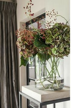 a vase filled with flowers sitting on top of a wooden table next to a mirror