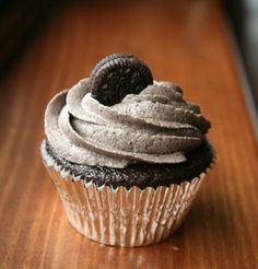 a cupcake with chocolate frosting and an oreo cookie on top sitting on a wooden table