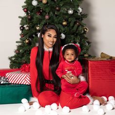 a woman sitting next to a baby in front of a christmas tree