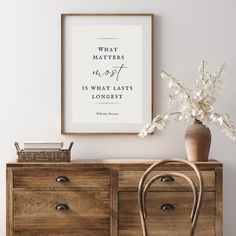 a wooden dresser topped with a vase filled with flowers next to a framed quote on the wall