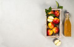 a crate filled with apples next to a bottle of apple cider