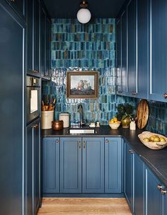 a kitchen with blue cabinets and wood flooring next to a painting on the wall