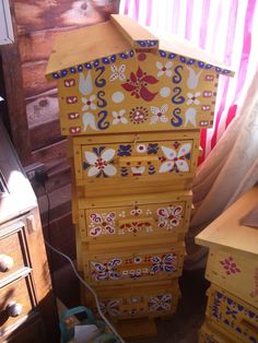 an old dresser is painted yellow and has colorful designs on the top, along with other drawers