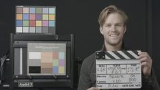 a man holding up a clapper in front of a camera and color swatches