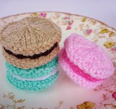 three small crocheted hamburgers are on a plate with pink, blue and green yarn