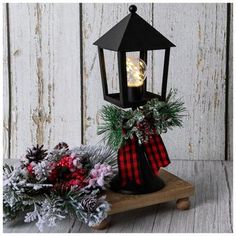 a black lantern with a red and white bow on it next to some evergreen branches