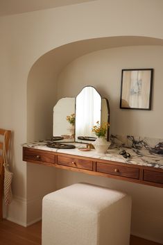 a vanity with a mirror, stool and pictures on the wall