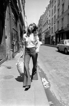 black and white photograph of woman walking down the street holding a basket in her hand