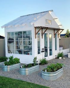 a small white house with lots of windows and plants in the front garden area,