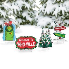 a group of street signs sitting in the snow next to some pine trees with snow on them