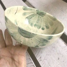 a hand is holding a green and white bowl