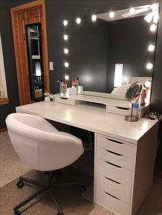 a white desk with lights on it and a chair in front of the mirror that is next to it