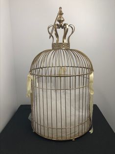 a golden birdcage sitting on top of a black table next to a white wall