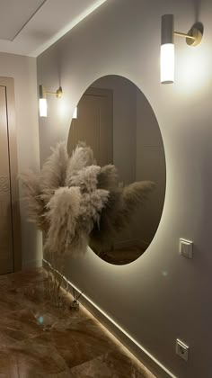 a bathroom with a round mirror and lights on the wall next to a vase filled with dry grass