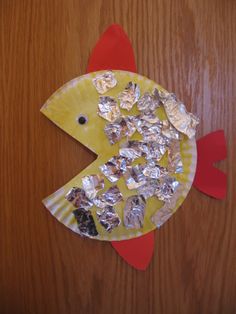 a fish made out of aluminum foil sitting on top of a wooden table next to a paper plate