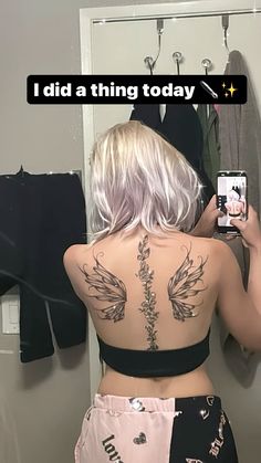 a woman taking a selfie in front of a mirror with tattoos on her back