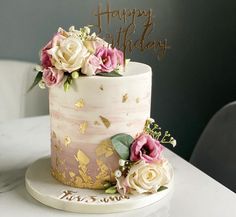 a pink and gold birthday cake with flowers on the top is sitting on a table