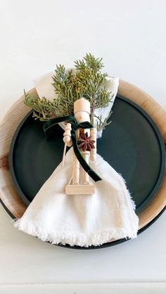 a table setting with napkins and an evergreen decoration on the top, along with a black plate