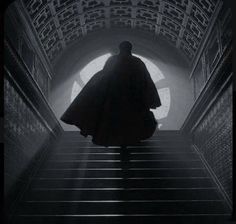 a man with a cape walking up some stairs in front of a light at the end