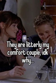 a man and woman sitting at a table in front of wine glasses with the caption, they are literally my comfort couple, i'dk why