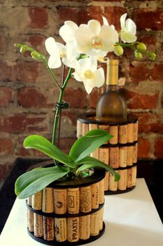 two wine cork vases with flowers in them on a table next to a brick wall