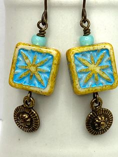 Adorable drop earrings of aqua and soft yellow pressed glass square beads in a sunburst pattern, highlighted by pattern brass charms. Non-allergenic niobium French wires. 1 3/8 inch drop from wire. Shown with Whooo Loves Owls bracelet trio, listed separately. Yellow Bohemian Rectangular Jewelry, Yellow Rectangular Bohemian Jewelry, Bracelet Trio, Sunburst Pattern, Owl Bracelet, Colorful Frames, Square Beads, Pretty Jewelry, Soft Yellow