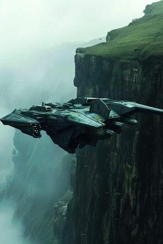 a sci - fi fighter jet flying over the edge of a cliff in front of foggy mountains