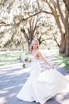 a woman in a white wedding dress is walking down the street with her bouquet on her hand