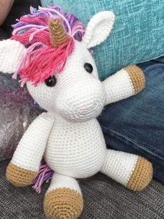 a crocheted stuffed unicorn sitting on top of a couch next to a pillow