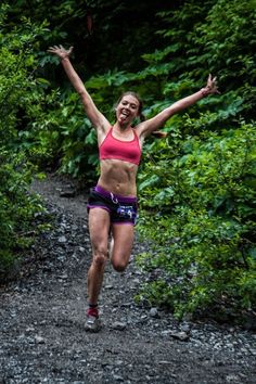 a woman running on a trail in the woods with her arms up and hands out