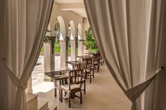 an outdoor dining area with white curtains and wooden tables in front of the patio doors