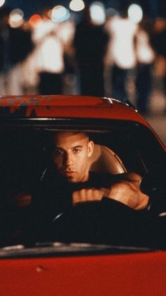 a man sitting in the driver's seat of a red sports car at night