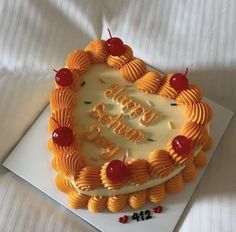 a birthday cake with orange icing and cherries on top, sitting on a white sheet