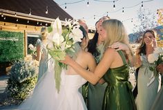 two women in green dresses are hugging each other while another woman is standing behind them