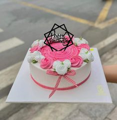 a birthday cake with pink frosting and white flowers on top is being held by someone's hand