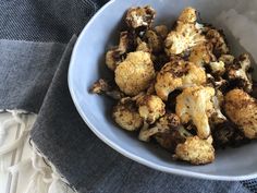 a white bowl filled with cooked cauliflower on top of a blue table cloth