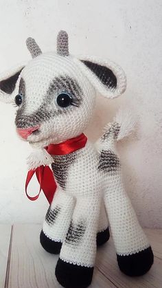 a knitted toy cow with a red ribbon around its neck sitting on a table