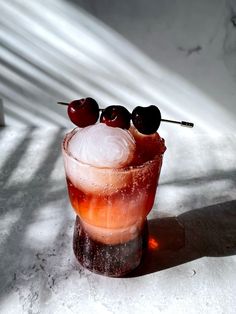 an alcoholic cocktail with ice and cherries on the rim, sitting in the sun