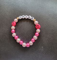 a pink and white beaded bracelet with smiley face charms on it's side