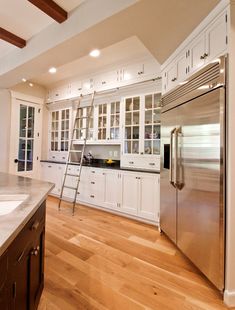 a ladder is in the middle of a kitchen with white cabinets and wood flooring