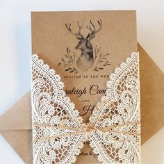 the wedding card is decorated with lace and a deer's head, on top of a brown envelope