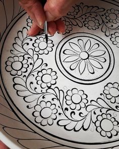 a person is drawing on a white plate with black and white designs in the center