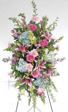 a bunch of flowers that are on top of a tripod stand in front of a white wall