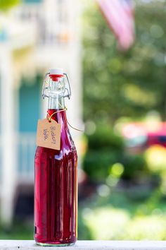 a bottle filled with red liquid sitting on top of a wooden table in front of a house