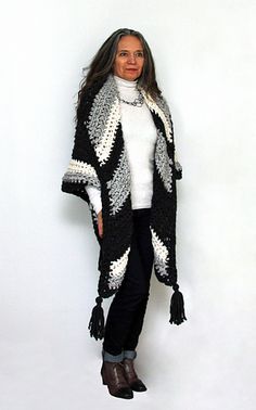 a woman standing in front of a white wall wearing a black and white crocheted shawl