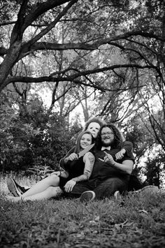 three people sitting on the ground in front of trees with one woman holding her child