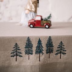 a table topped with a red truck next to a forest filled with pine trees on top of a cloth covered table