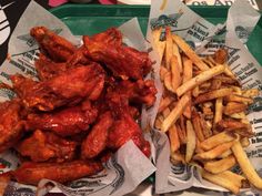 two trays filled with chicken wings and french fries on top of paper wrappers