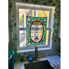 a stained glass window hanging from the side of a kitchen sink in front of a window