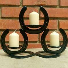 three white candles are placed in front of a brick wall with horseshoes on it